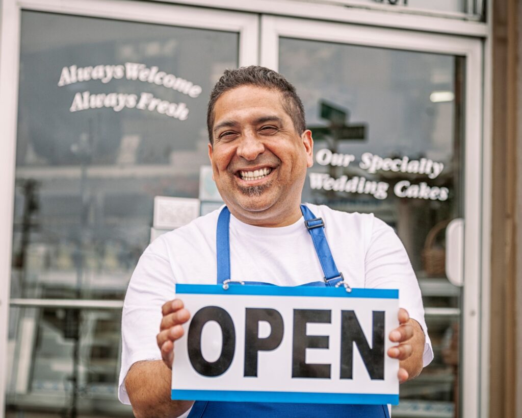 man holding an open sign in front of his business