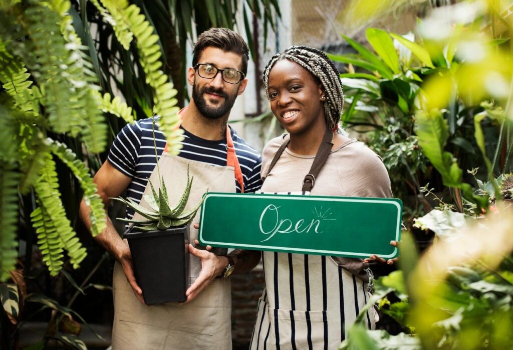 Man and woman holding an open sign at a plant nursery.