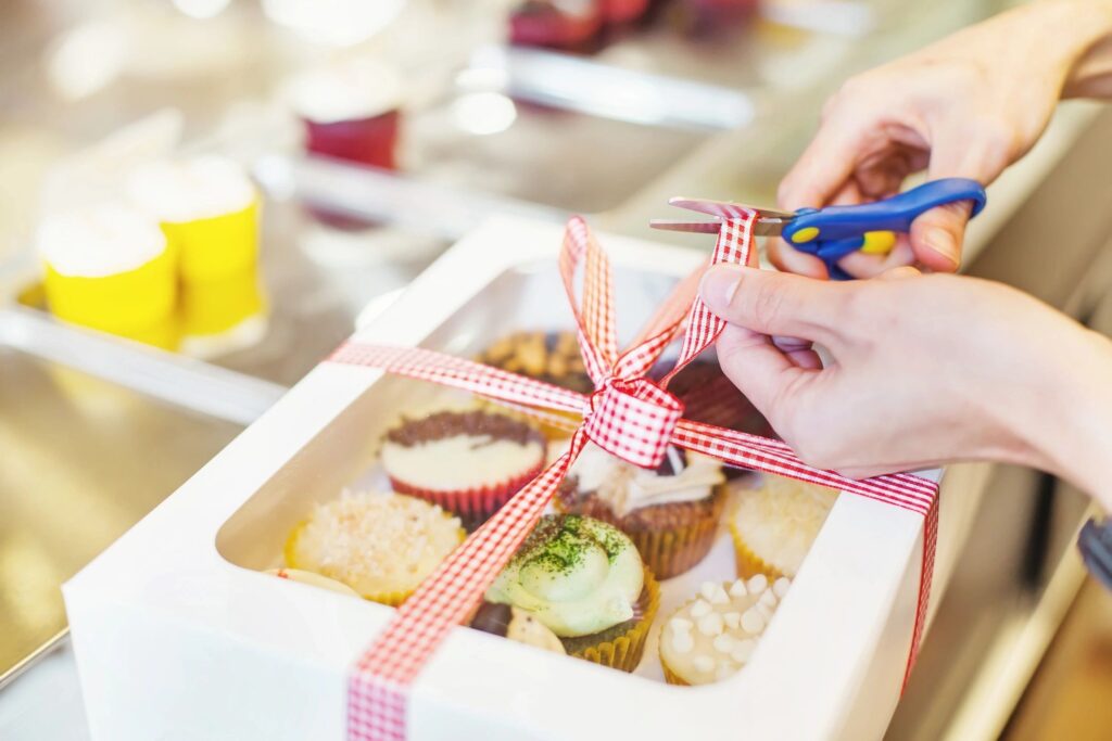 Woman cutting a ribbon on a box of baked goods. Pros and cons of owning a bakery